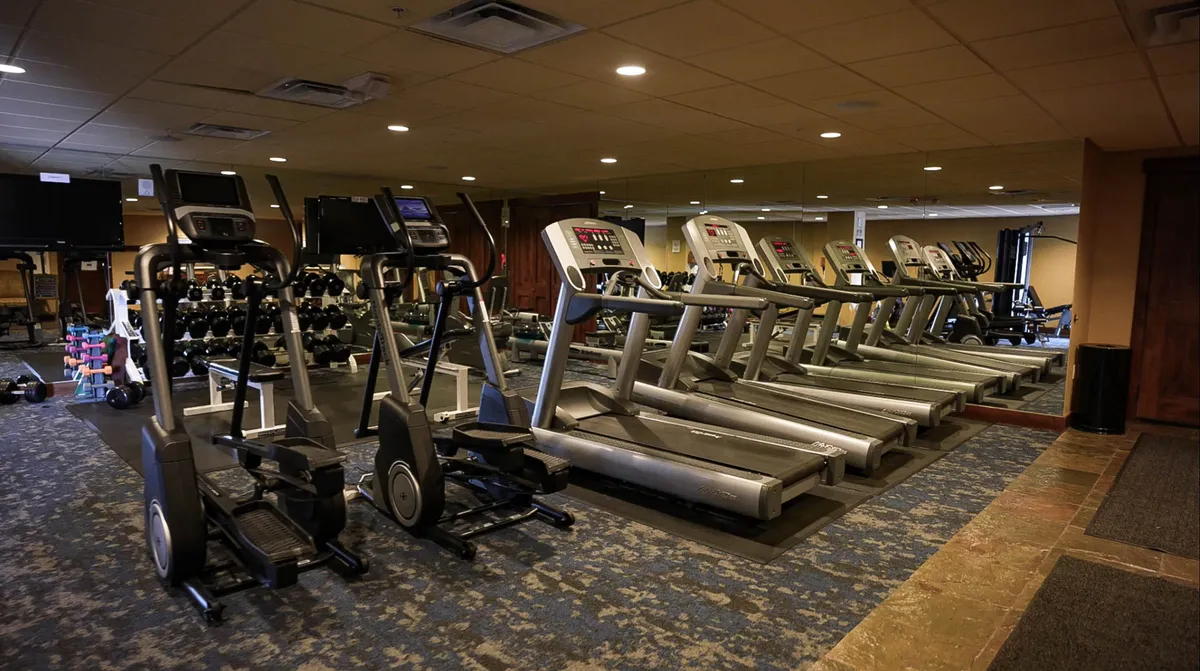 An interior fitness center filled with modern workout equipment, including ellipticals, treadmills, dumbbells, and a mirrored wall. The space is bright, open, and designed for motivation, perfect for guests looking to stay active during their stay.
