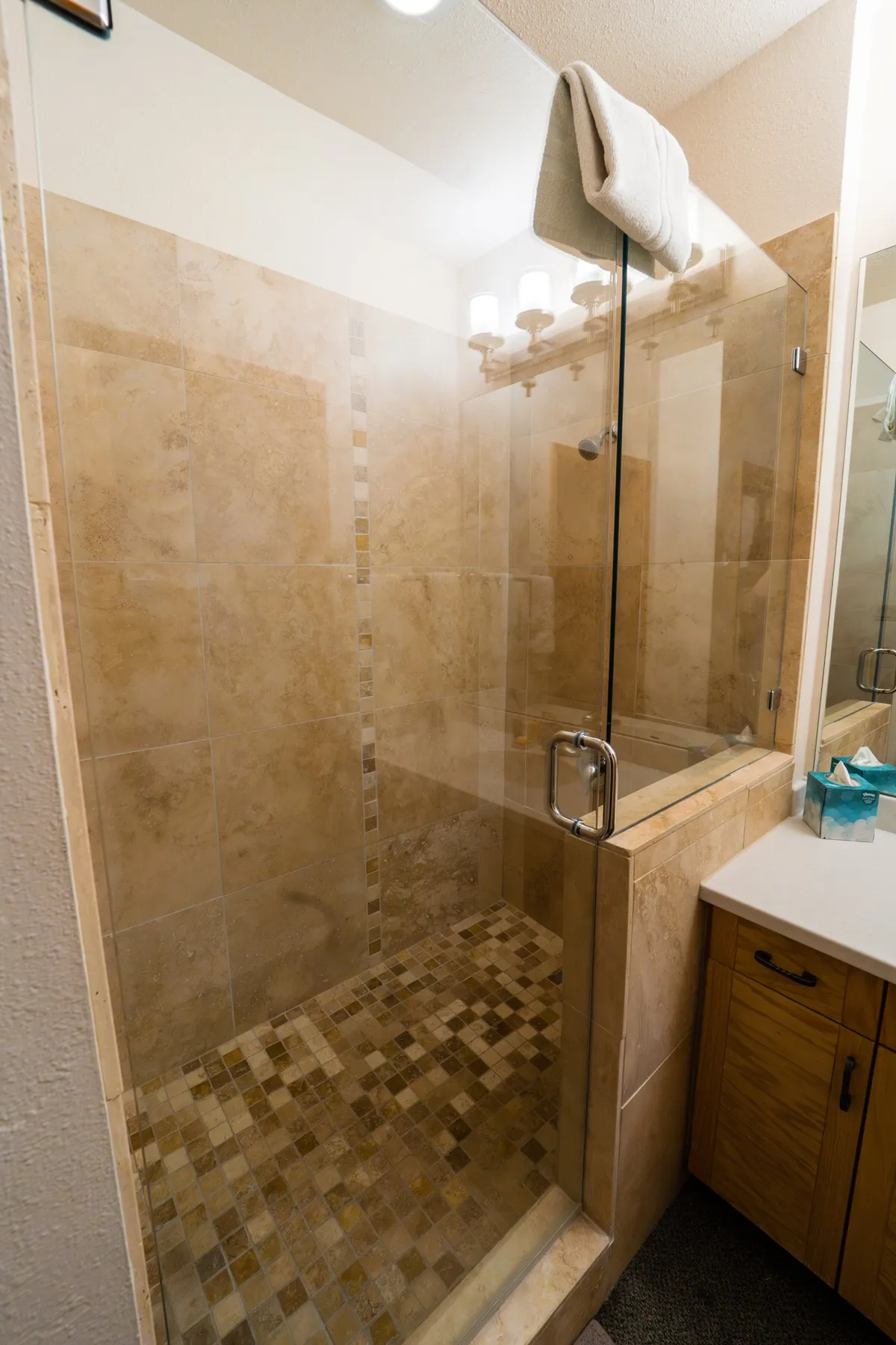 A stylish bathroom scene with a glass shower enclosure, textured tiles, and a towel neatly arranged on the rack. The space is serene and designed for relaxation after a day of adventure.