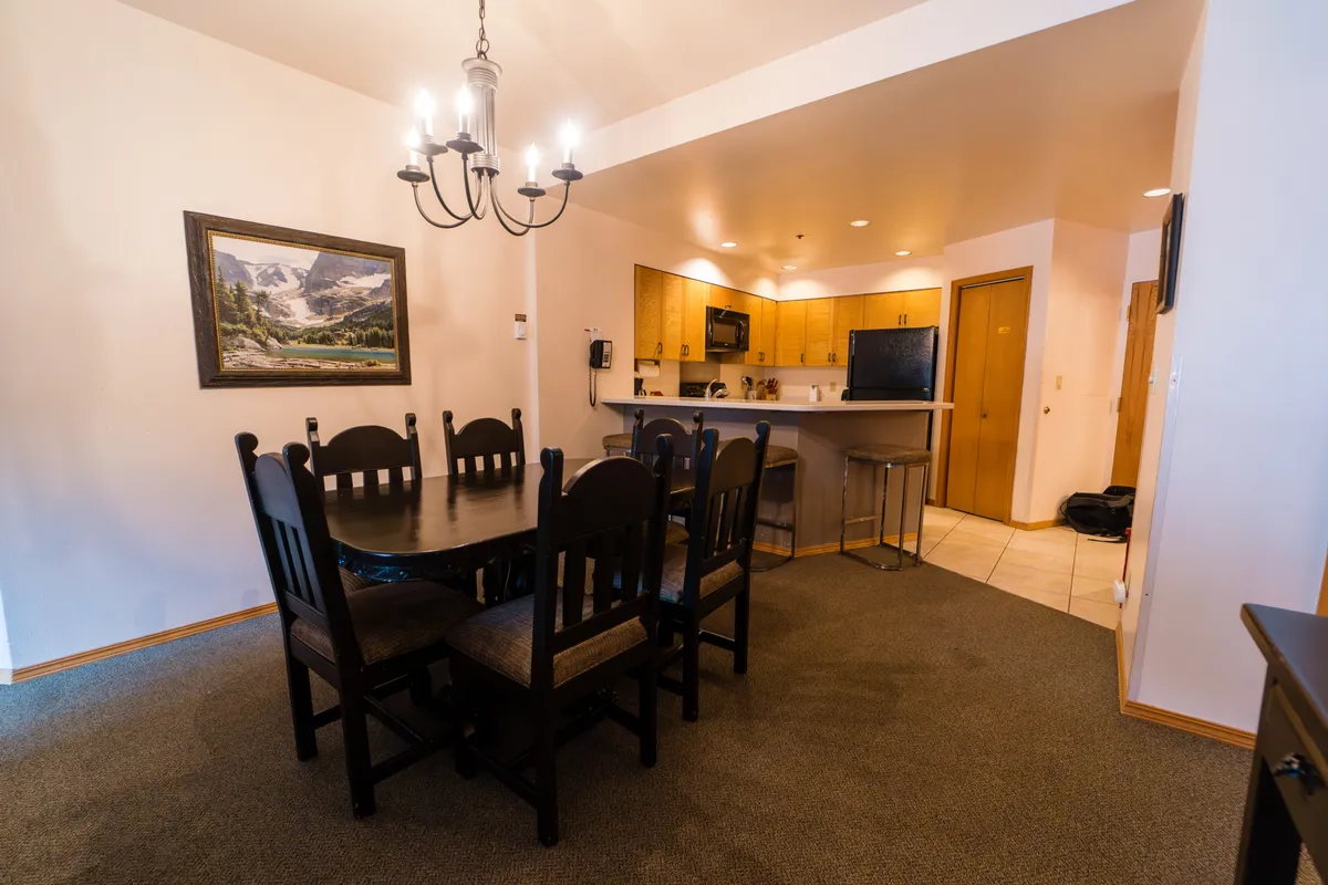 A cozy dining area adjacent to the kitchen, featuring a chandelier, dining table, and a glimpse of the kitchen beyond. The space is set for family meals, gatherings, or intimate dinners, with warm lighting and inviting decor.