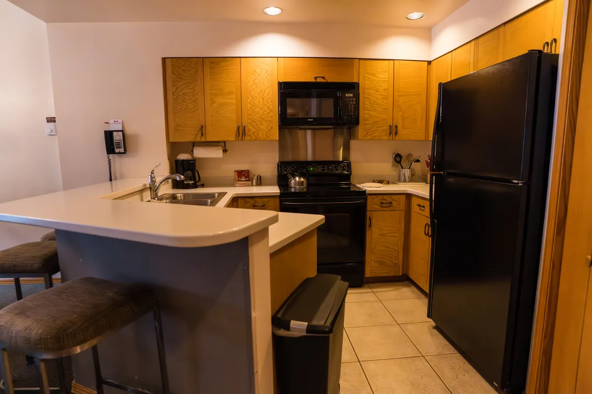 A well-lit kitchen space featuring a central island, sleek black refrigerator, stainless steel microwave, and warm wood cabinetry. The island offers ample prep space and serves as a natural gathering spot for cooking and socializing. The modern appliances and design invite collaborative meal prep and relaxed conversation.