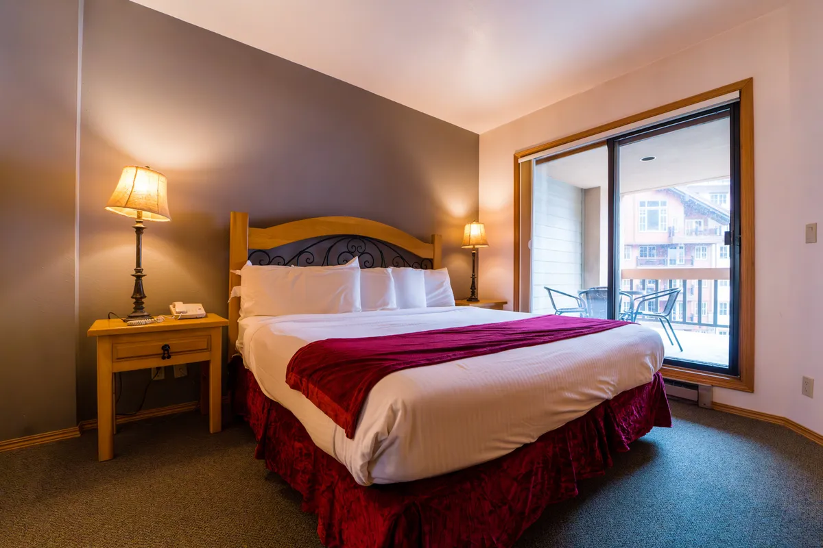 A bright and inviting bedroom with a comfortable bed, bedside lamps, a window that lets in natural light, and a nightstand. The scene conveys warmth and tranquility, ideal for relaxation and a good night's sleep.