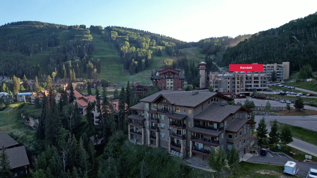 A scenic exterior view featuring residential buildings set against a stunning mountain backdrop, with a visible parking area in the foreground. The natural landscape suggests easy access to outdoor activities like hiking and relaxation while providing a sense of tranquility.