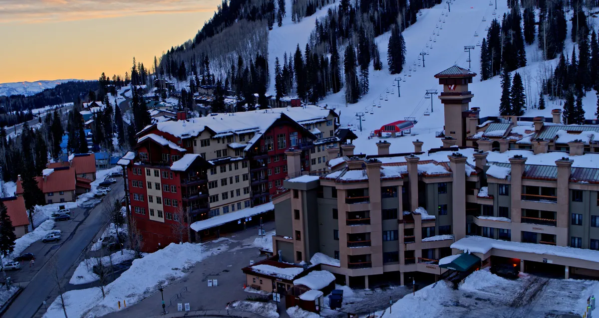 A sweeping view of snow-covered mountains, ski lifts, cozy resort lodges, and evergreen trees, capturing the essence of the San Juan Mountains and the vibrant village atmosphere. The image hints at adventurous activities like skiing or snowshoeing, as well as après-ski relaxation.