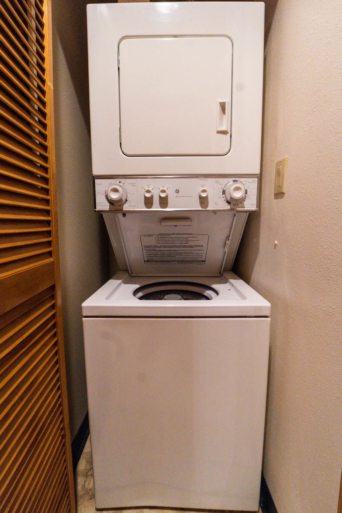 A compact, practical laundry area featuring a stacked washer and dryer behind wooden louvered doors. This convenient setup is essential for guests seeking extended stays or added comfort during their visit.