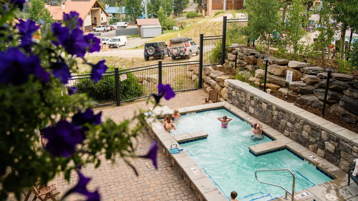 This vibrant exterior image showcases a heated swimming pool and inviting hot tub nestled amid lush landscaping and vibrant flowers. The space is designed for relaxation and socializing, with comfortable seating and a scenic backdrop that encourages guests to unwind and enjoy resort-style amenities.