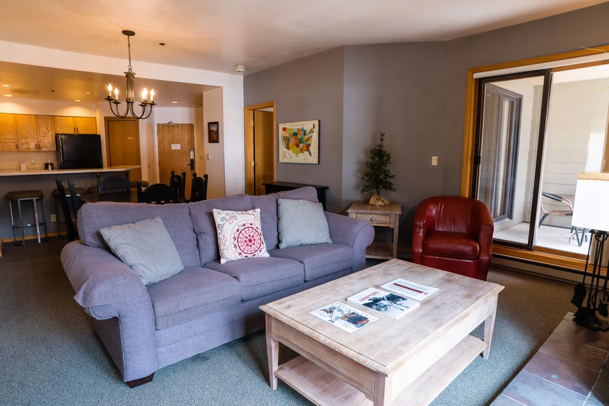 A warm, inviting living room with a sofa adorned with decorative pillows, a wooden coffee table, a red armchair, and a small Christmas tree. Artwork on the wall and abundant natural light contribute to a welcoming, communal feel, ideal for group relaxation or festive gatherings.