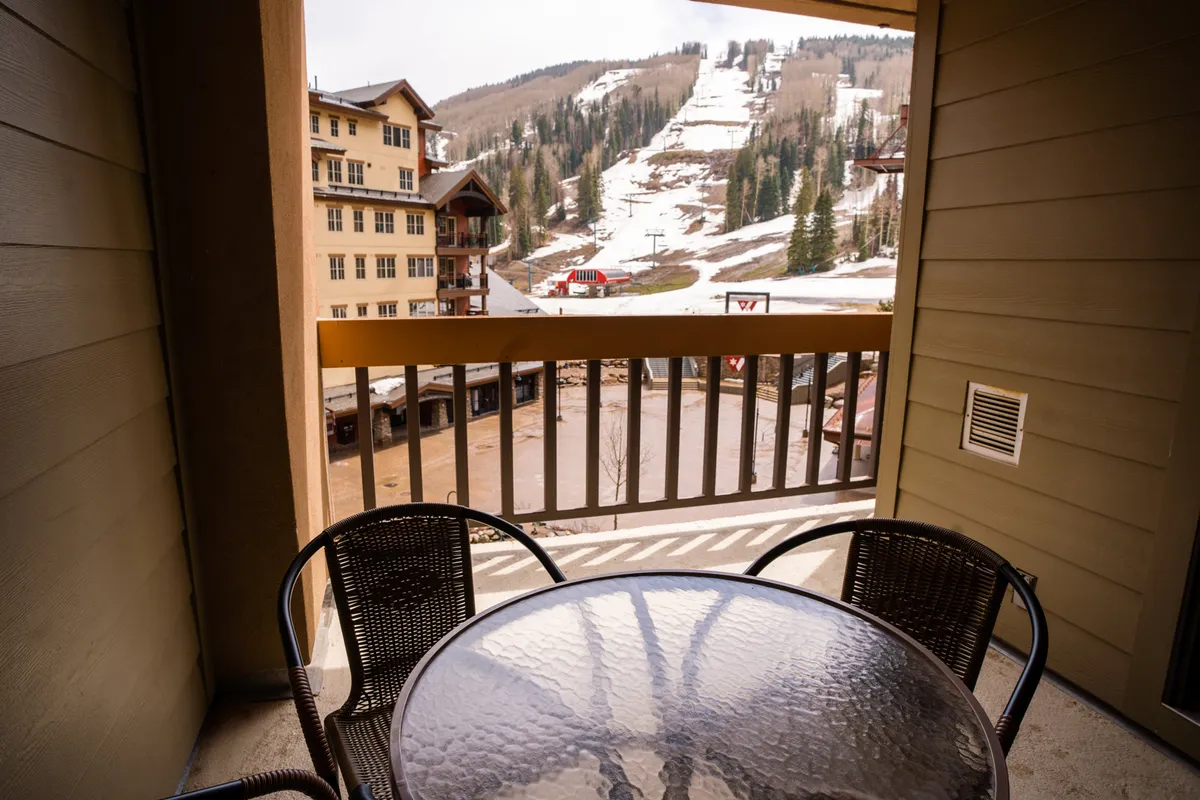 This image features a balcony setup with a table and chairs, looking out over stunning mountain scenery and ski slopes. The setting evokes a sense of privacy and serenity, ideal for couples or small groups seeking a tranquil moment together. The view suggests both daytime relaxation and the possibility of witnessing vibrant sunsets.
